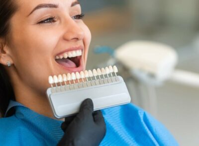 A beautiful young patient uses a dental tooth shade guide for whitening teeth service to ensure a perfect choice of color. Bleaching, prosthetics, orthopedic dentistry concept.